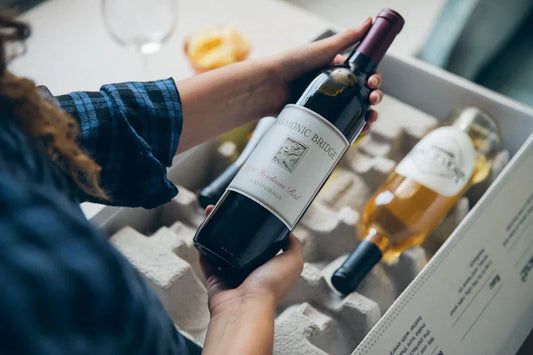 A woman holding a bottle of red wine over a box of Firstleaf wine.