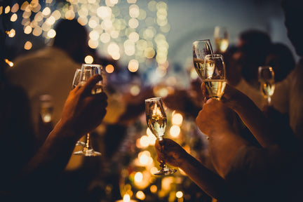 People toasting glasses of prosecco with glittering lights in the background.