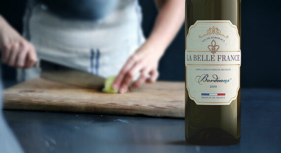La Belle France 2019 Bordeaux Blanc Bordeaux AOP, France with a blurred person cutting food on a cutting board in the background