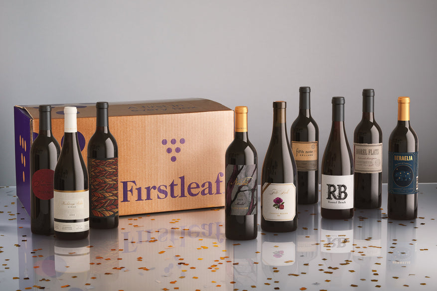 9 bottles on a confetti covered floow with a firstleaf box on white background.