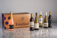 6 bottles of wine on a confettig covered floow with a Firstleaf box on a white background