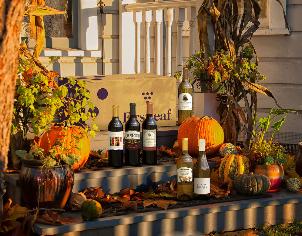 A Firstleaf box and bottles of wine on a porch with leaves and pumpkins. 