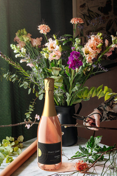 Punt Comú NV Cava Brut Rosé DO Cava, Spain on a table next to someone preparing a bouquet. 