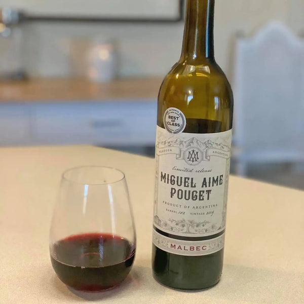 Bottle and glass of Miguel Aime Pouget Malbec wine on a kitchen counter.