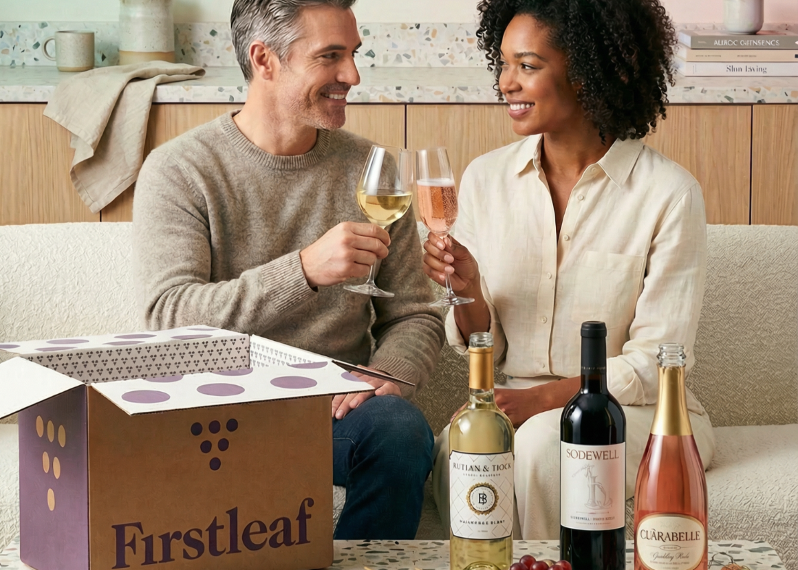 Graphic, an open Firstleaf box, six bottles of wine, and a fruit and cheese platter sitting on a kitchen counter.
