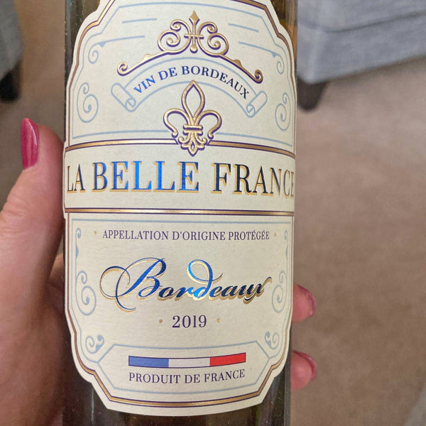 Bottle of La Belle France Bordeaux wine held by a hand with pink nail polish.