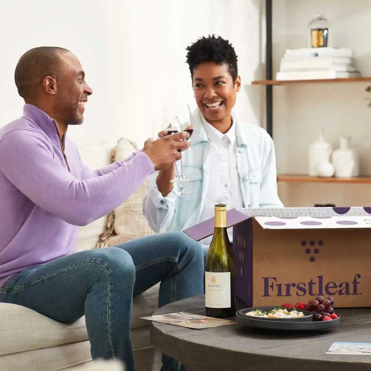 Two people sitting on a couch with a bottle of wine and a 'Firstleaf' box in a living room setting.