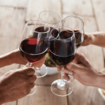 Four people toasting with red wine glasses in a warm indoor setting.