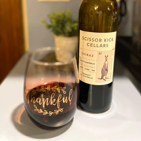 Bottle of Scissor Kick Cellars Shiraz wine with a glass labeled 'Thankful' on a surface.